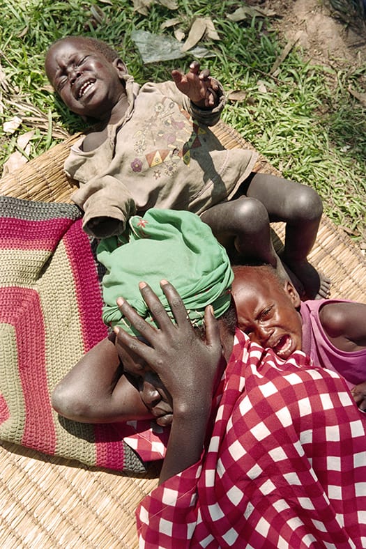 5-June-2004-An-exhausted-Rwandan-mother-lies-next-to-her-two-crying-children-at-Runango-refuge...jpg